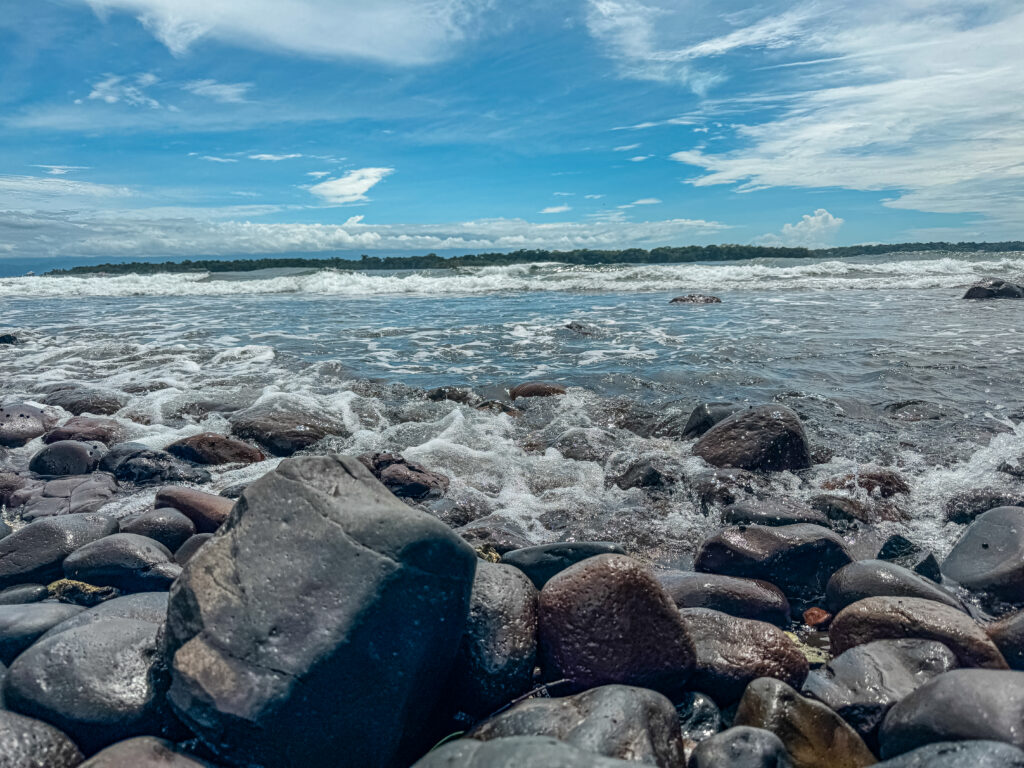 The rugged, rocky coastline of Isla Bastimentos, Panama, with ocean waves crashing against dark rocks on the shore.