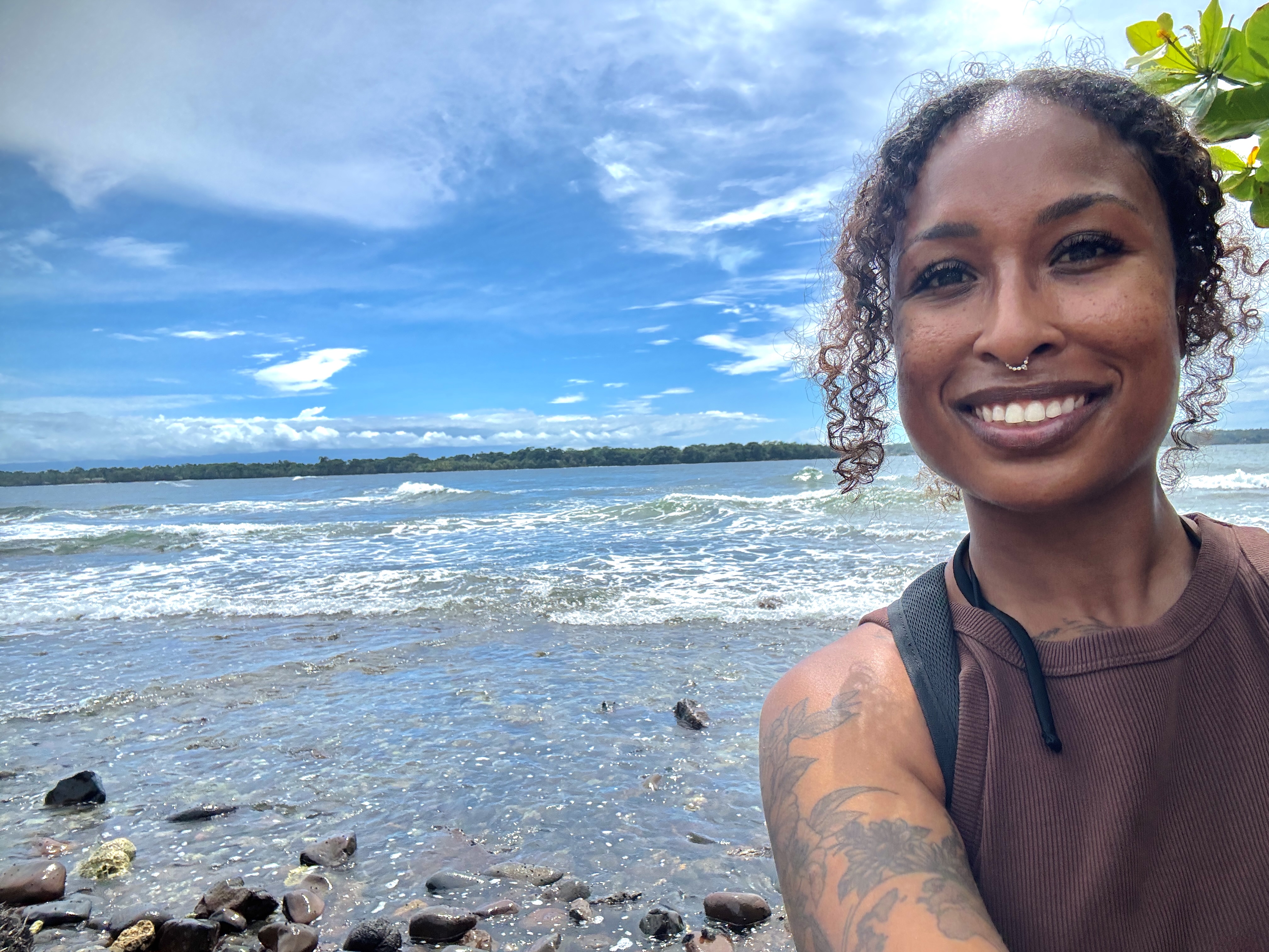 solo black female traveler at the rugged, rocky coastline of Isla Bastimentos, Panama, with ocean waves crashing against dark rocks on the shore.