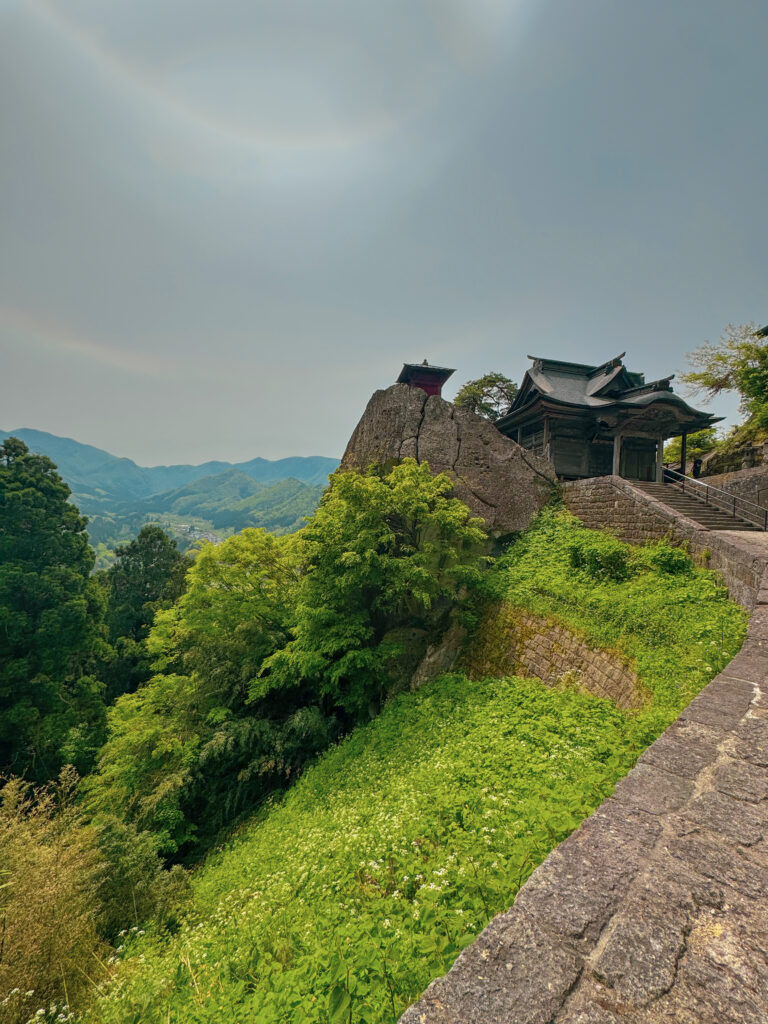 Historic red Nokyodo hall and Kaizando perched precariously on a rocky cliffside peak at Yamadera Temple
